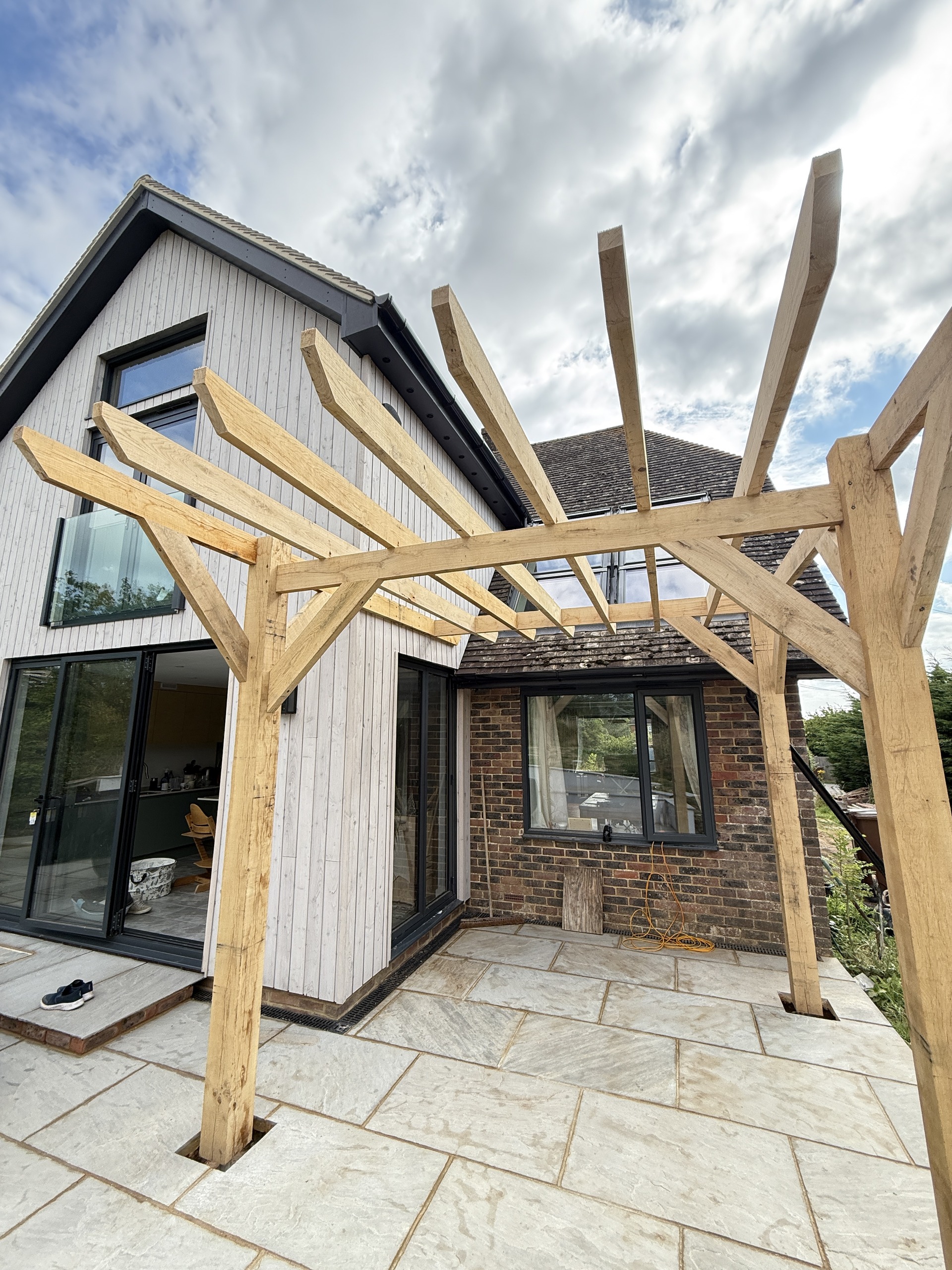 Finished green oak pergola with braced posts beside a house and patio